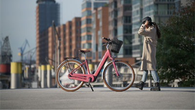 A woman runs toward a pink Cube Ella Hybrid e-bike in a city.