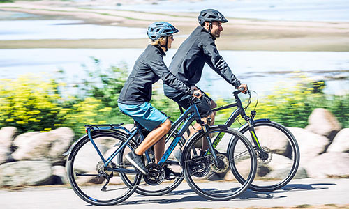 A man and a woman ride trekking bikes along the seashore.