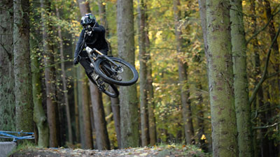 Cyclist wearing a full-face helmet jumps high with a Cube Stereo ONE77 Fully mountain bike.