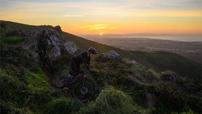 Two cyclists ride down a mountain, each on a Cube Stereo Fully mountain bike