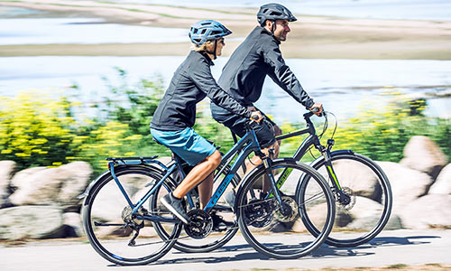A man and a woman ride trekking bikes along the seashore.