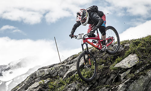 Downhill cyclist wearing a full-face helmet rides down a rocky mountain.