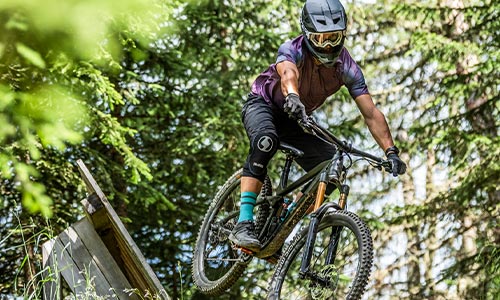 Cyclist wearing a full-face helmet rides a full-suspension mountain bike through the forest.