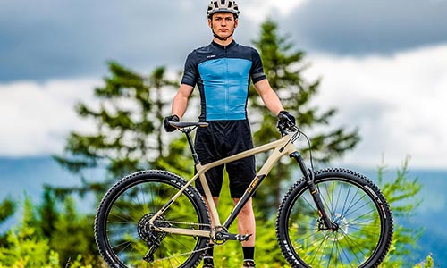 Man in cycling gear standing behind a hardtail mountain bike.