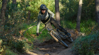 Cyclist riding diagonally through the forest on a Cube Stereo Fully mountain bike.