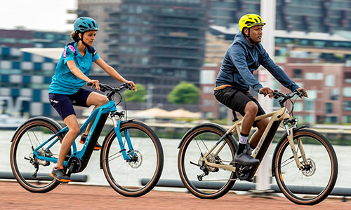 A man and a woman are riding on a bike path with a big city in the background.