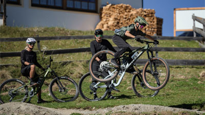 A child jumps with a Cube Stereo Fully mountain bike, two cyclists watch.