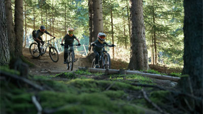 Two teenagers and a cyclist ride through the forest on Cube Stereo Fully mountain bikes.